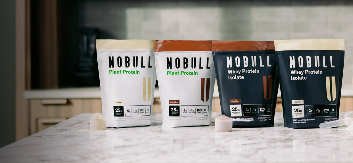 Four packages of Chocolate and Vanilla NOBULL protein products on a kitchen counter.