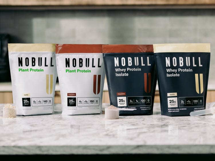 Four packages of Chocolate and Vanilla NOBULL protein products on a kitchen counter.