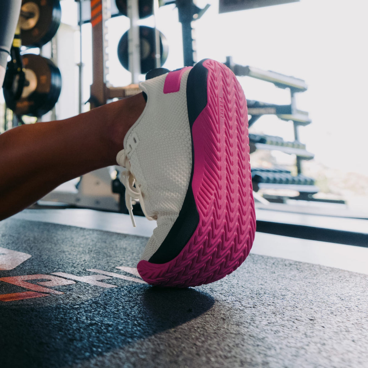 Close-up of a pink and white athletic shoe on a gym floor with weights in the background