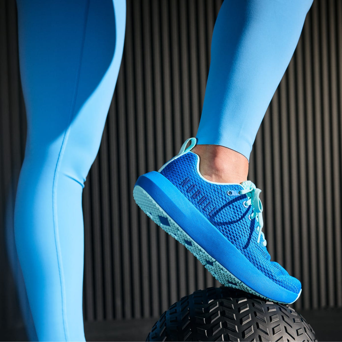 Person wearing blue athletic shoes and leggings on a black background