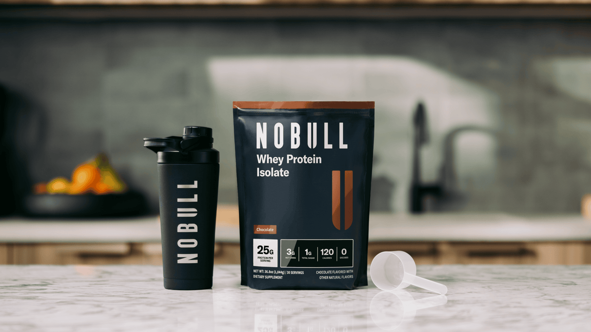 NOBULL chocolate whey protein isolate package and shaker cup on a kitchen counter.