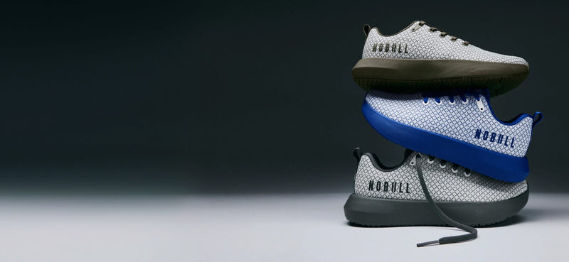 Three stacked athletic sneakers on a dark studio background. The top shoe is light gray with olive green soles and black 'MOBBULL' branding.