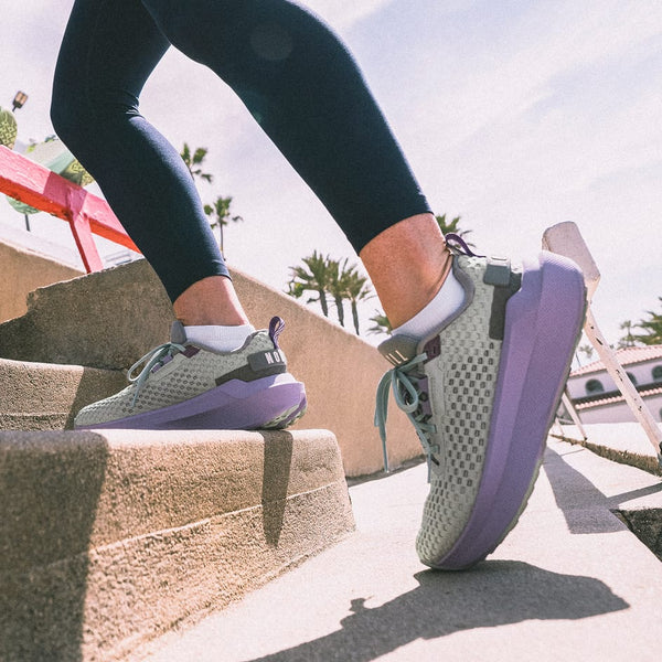 Person wearing gray and purple Journey 2 Shoes climbing stairs with palm trees in the background